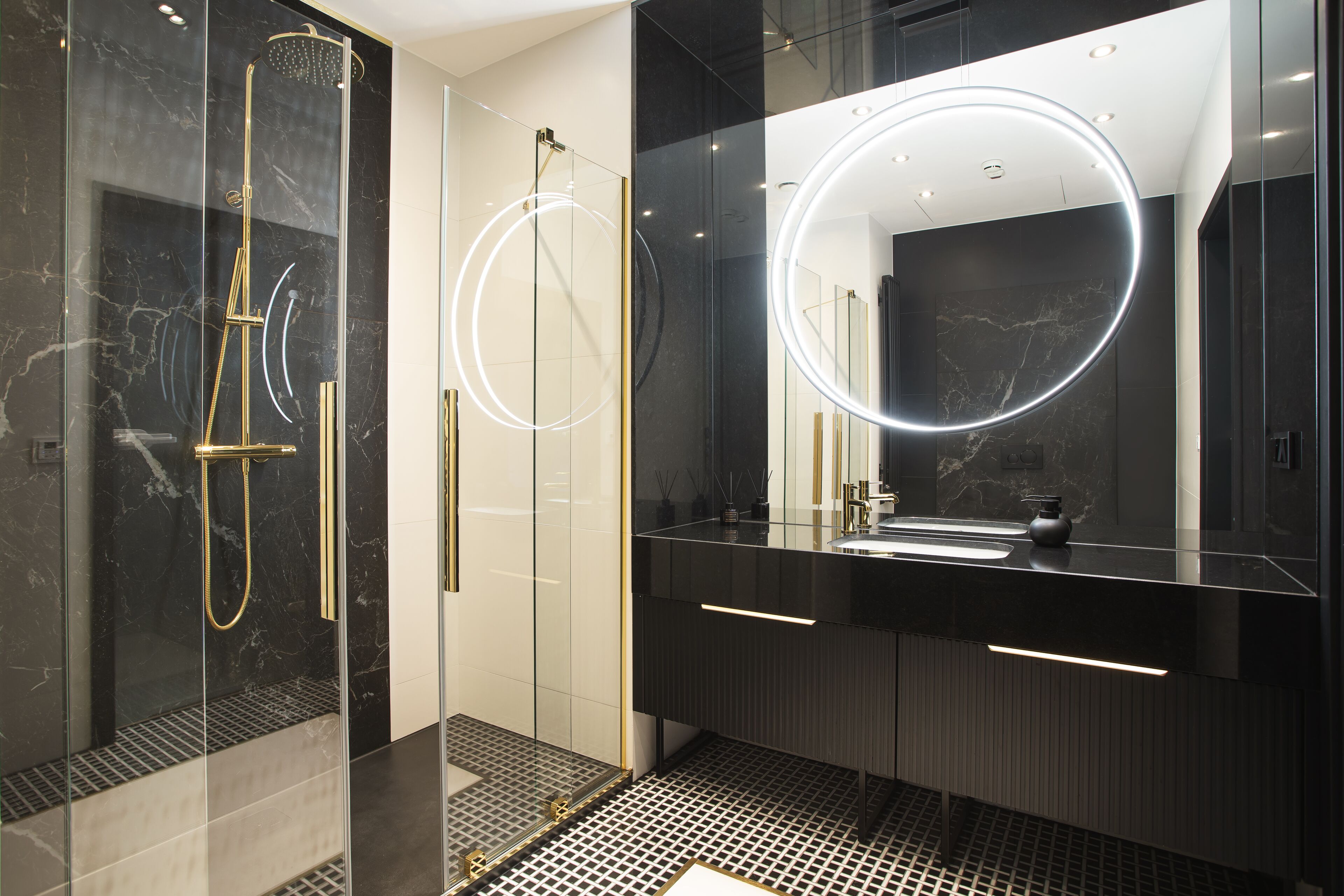 A modern bathroom with a glass-enclosed shower, a large mirror with a circular light, and a black vanity with a sink.