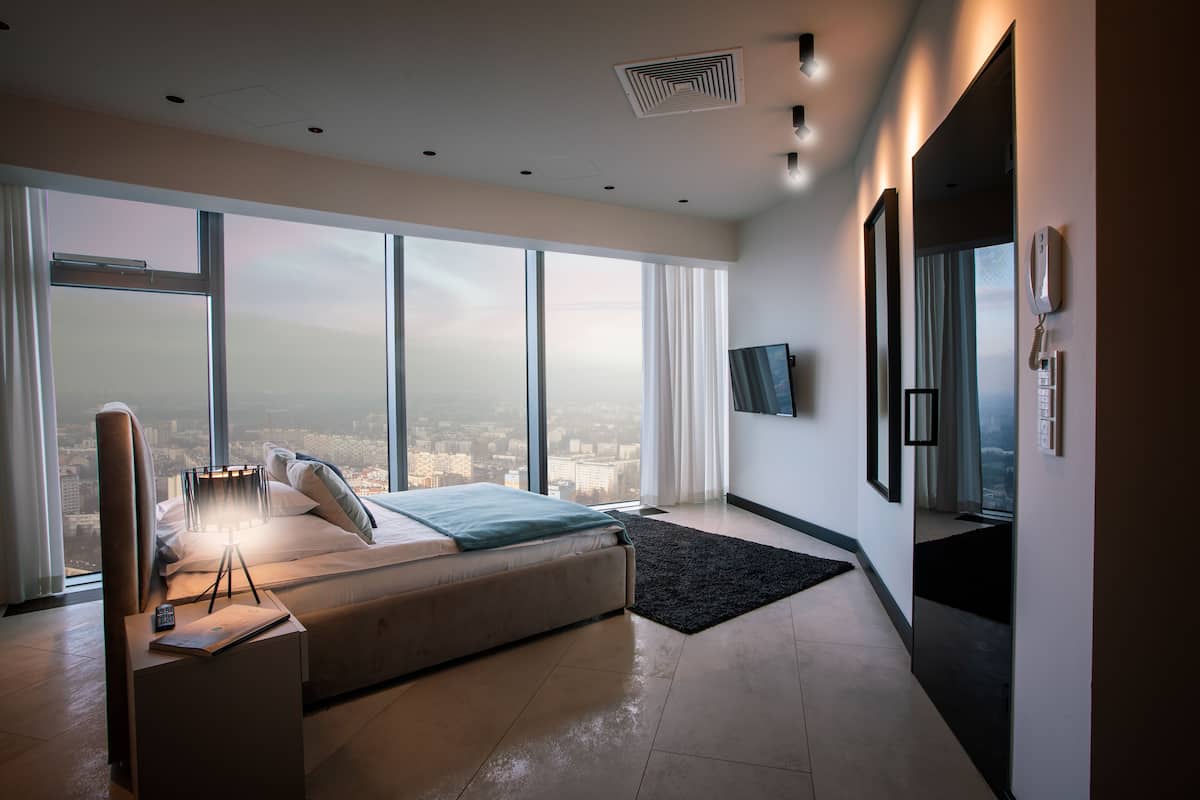 Ein modernes Schlafzimmer mit einem großen Bett, einem Schreibtisch und Blick auf die Stadt durch große Fenster.