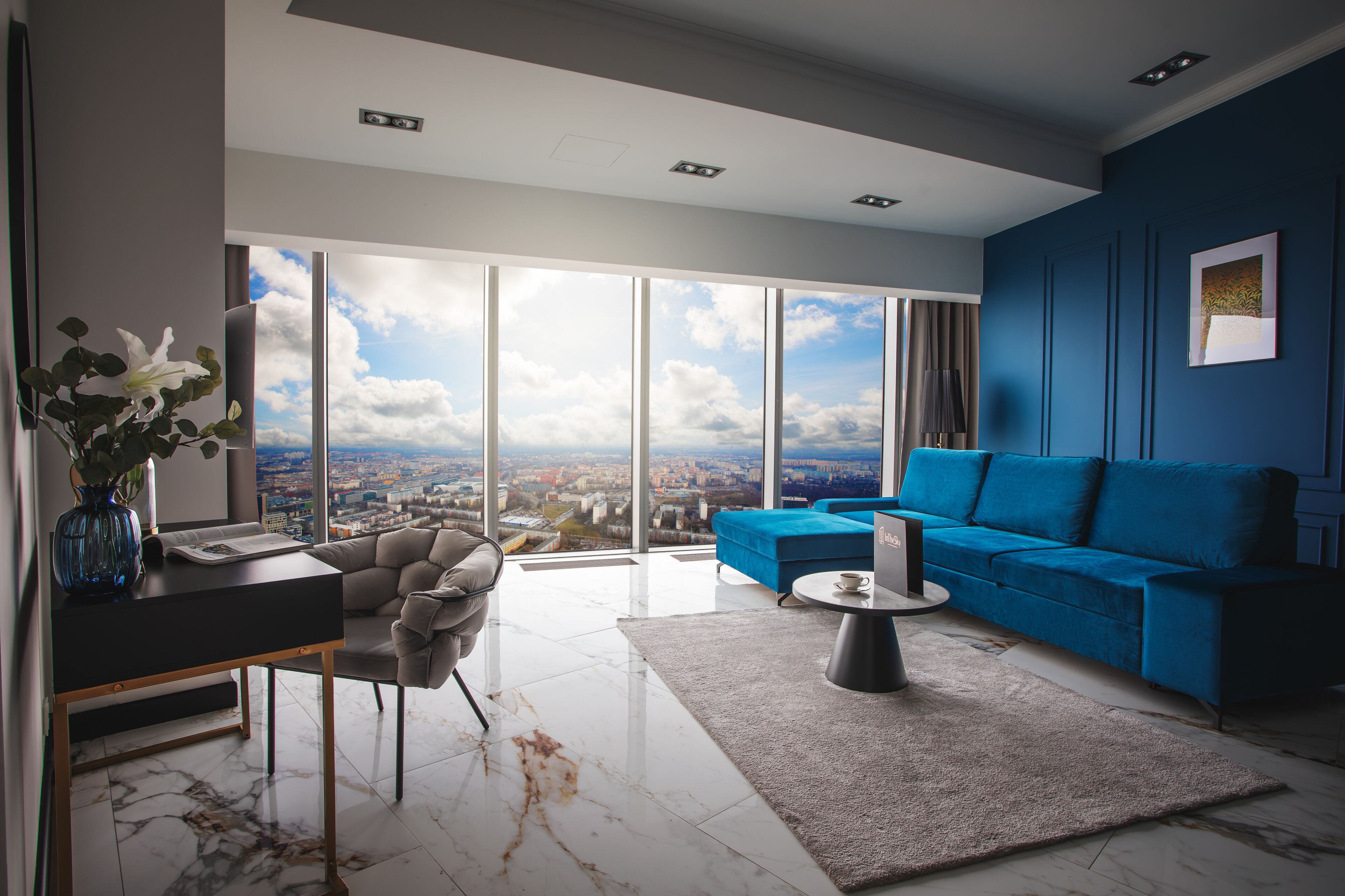 Una sala de estar moderna con vistas a la ciudad, un sofá azul, una mesa de centro y un escritorio con un florero.