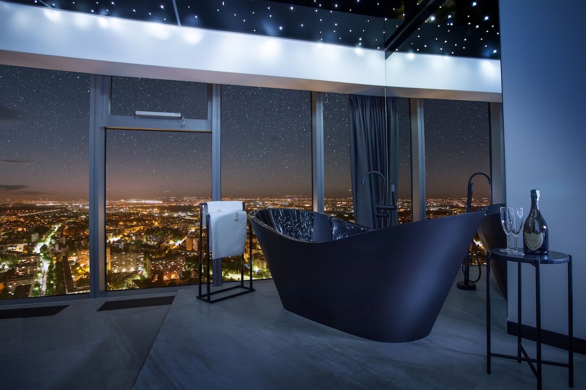 Ein modernes Badezimmer mit einer großen Badewanne, einem Handtuchhalter und einem Tisch mit einer Flasche und Gläsern.