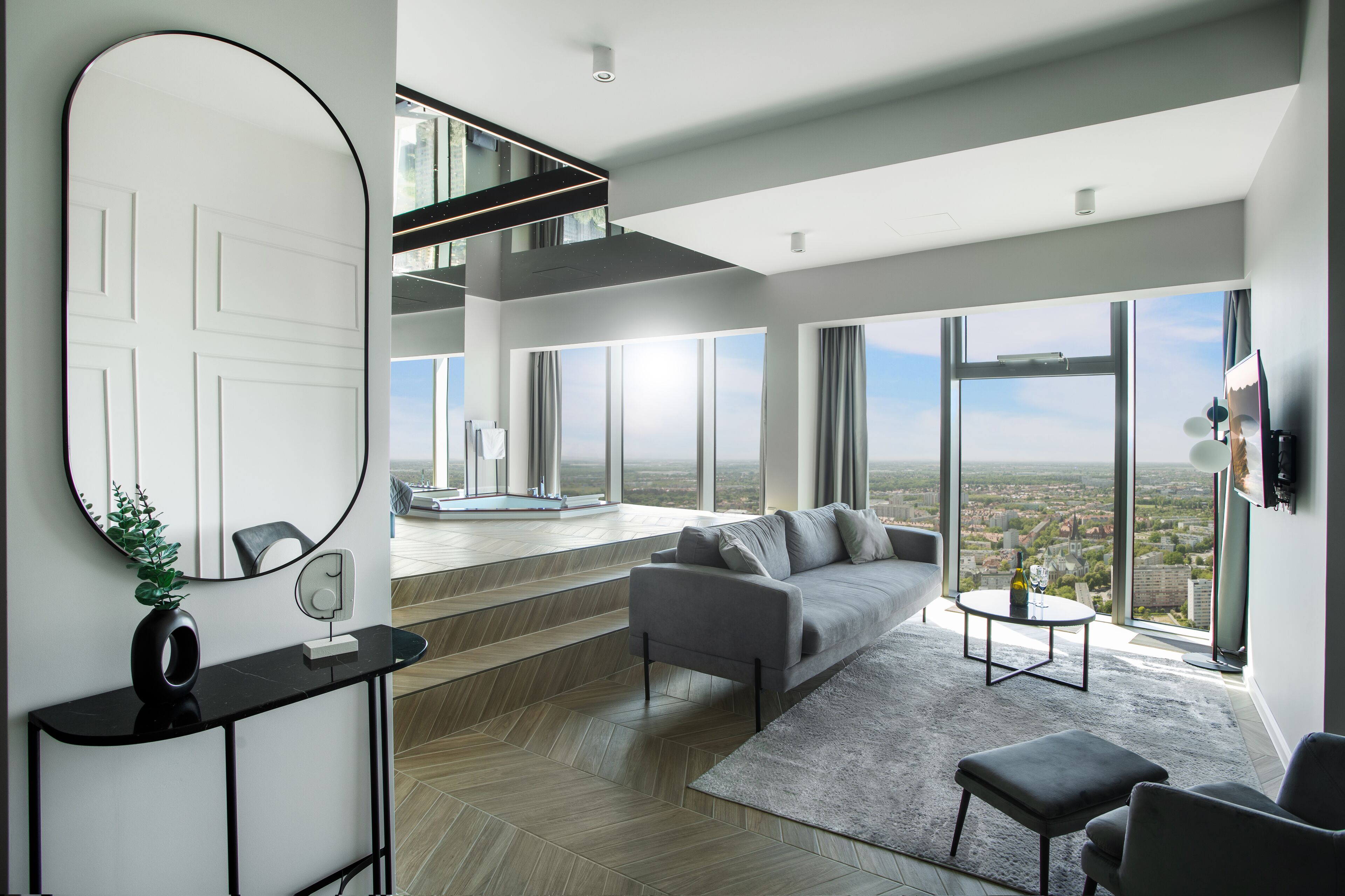 Een moderne woonkamer met een grijze bank, een ronde spiegel en uitzicht op de stad.