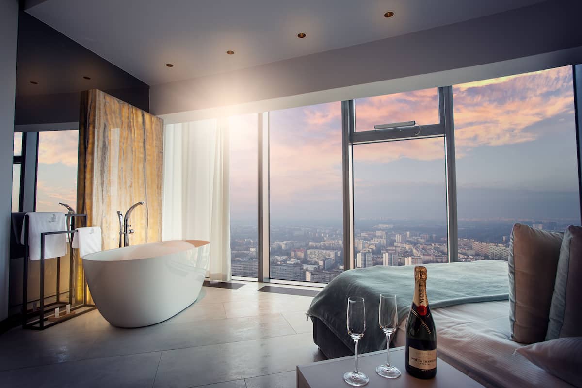 Ein modernes Badezimmer mit einer freistehenden Badewanne, einem großen Fenster mit Blick auf die Stadt und einer Champagnerflasche auf einem Tisch.