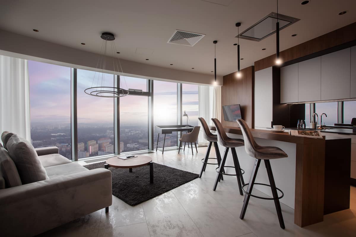 Ein modernes Wohnzimmer mit einer Couch, Couchtisch und Barbereich mit Hockern. Große Fenster bieten Blick auf die Stadt.
