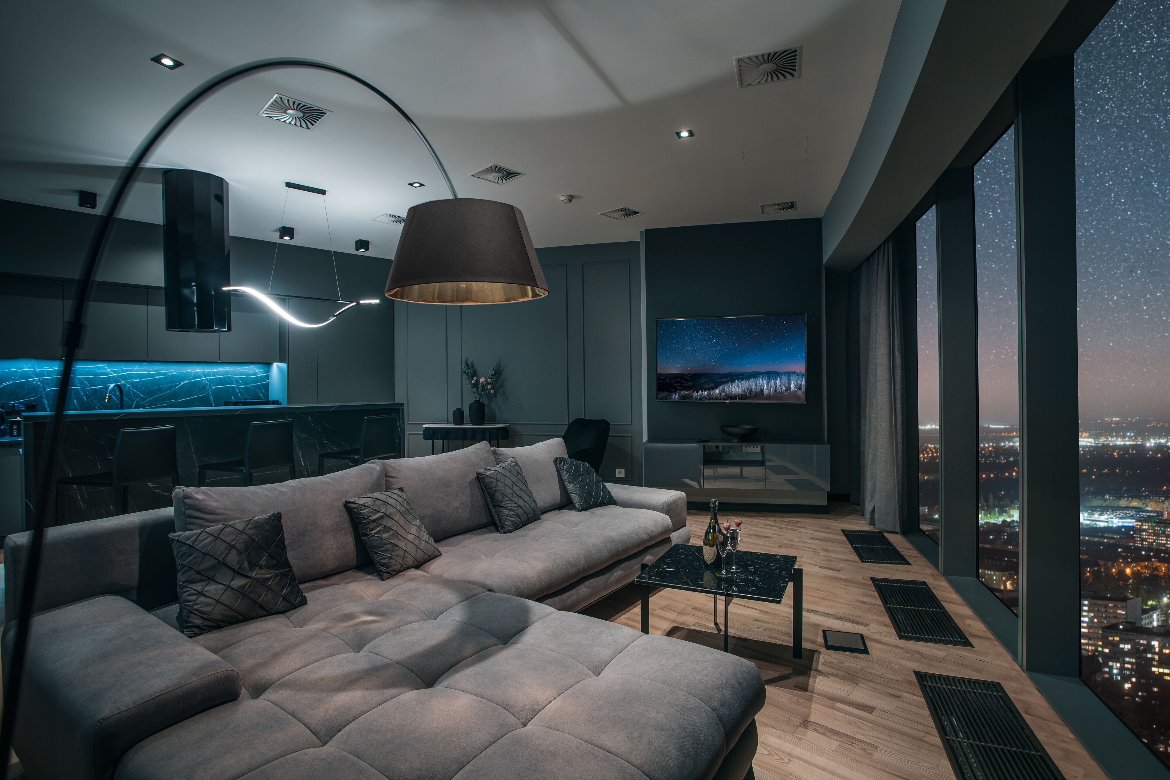A modern living room with a large sofa, a coffee table, and a city view through large windows.