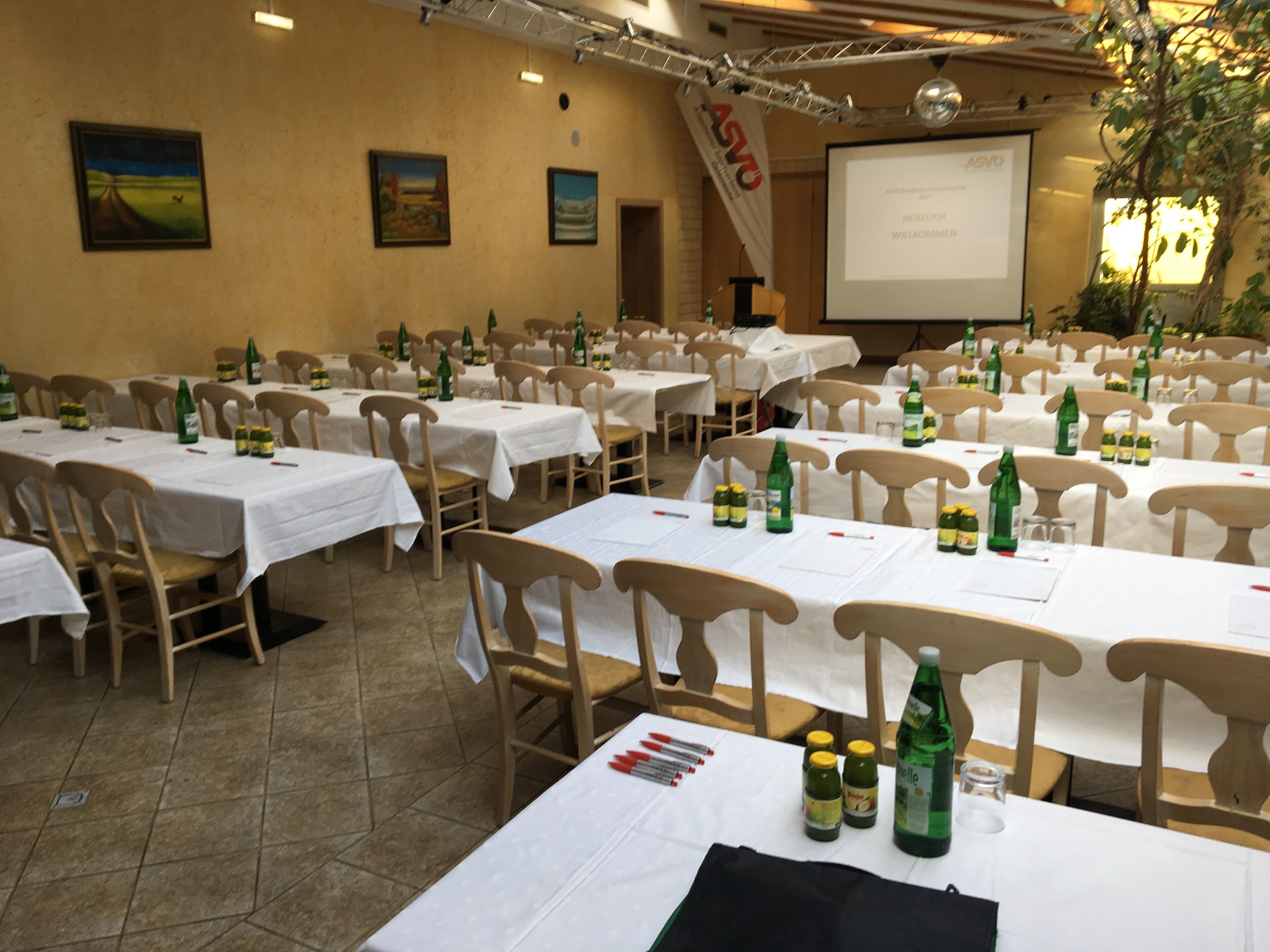 Ein Konferenzraum mit mehreren Tischen, Stühlen und einer Projektionsleinwand.