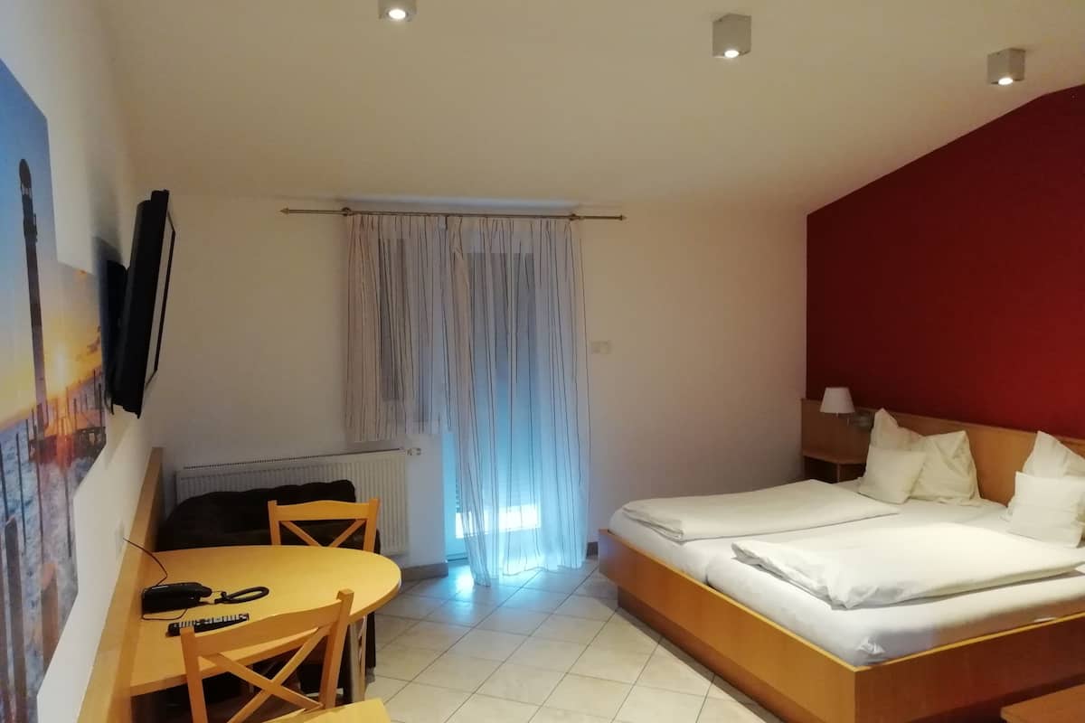 A hotel room with a bed, a desk with a chair, a television mounted on the wall, and a window with curtains.