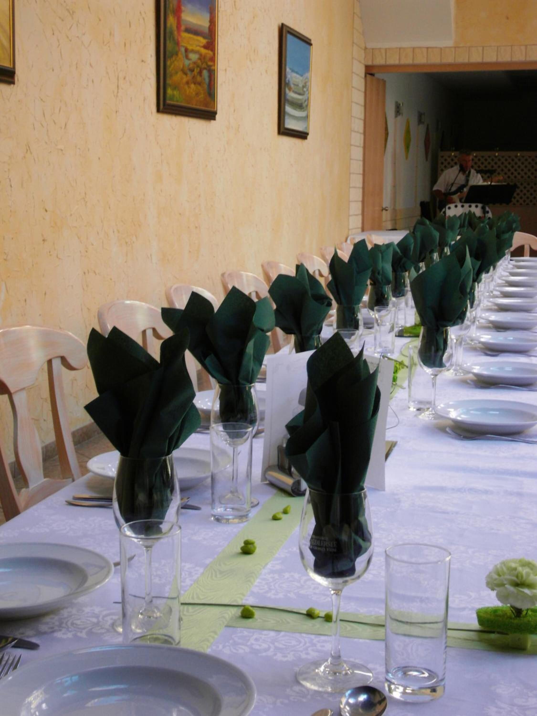 A long dining table set with white plates, green napkins, and clear wine glasses.