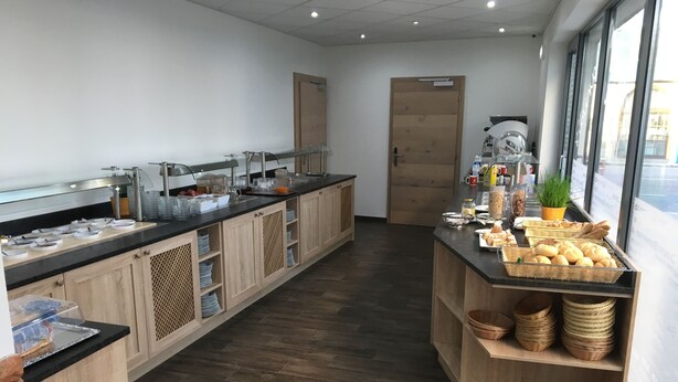 Een moderne keuken met houten kastjes, een zwart aanrecht en diverse ontbijtartikelen.