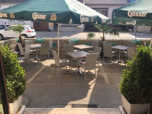 An outdoor cafe area with wicker tables and chairs, green umbrellas, and stone walls. - Weinhotel Kirchenwirt (Gols)