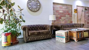 Een woonkamer met een bruine leren bank, een bijzettafeltje gemaakt van oude boeken, een Route 66 klok, een bakstenen muur en een potplant.