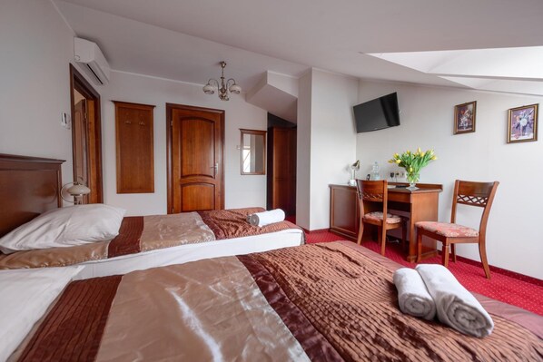 A hotel room with two beds, a desk, a chair, a television, and a red carpet.