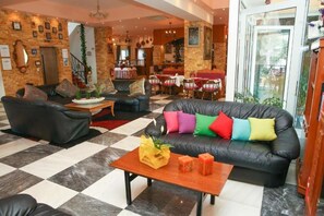 Un hall d’hôtel avec un sol à carreaux, des canapés en cuir, une table basse en bois et un bar situé au fond de la pièce.