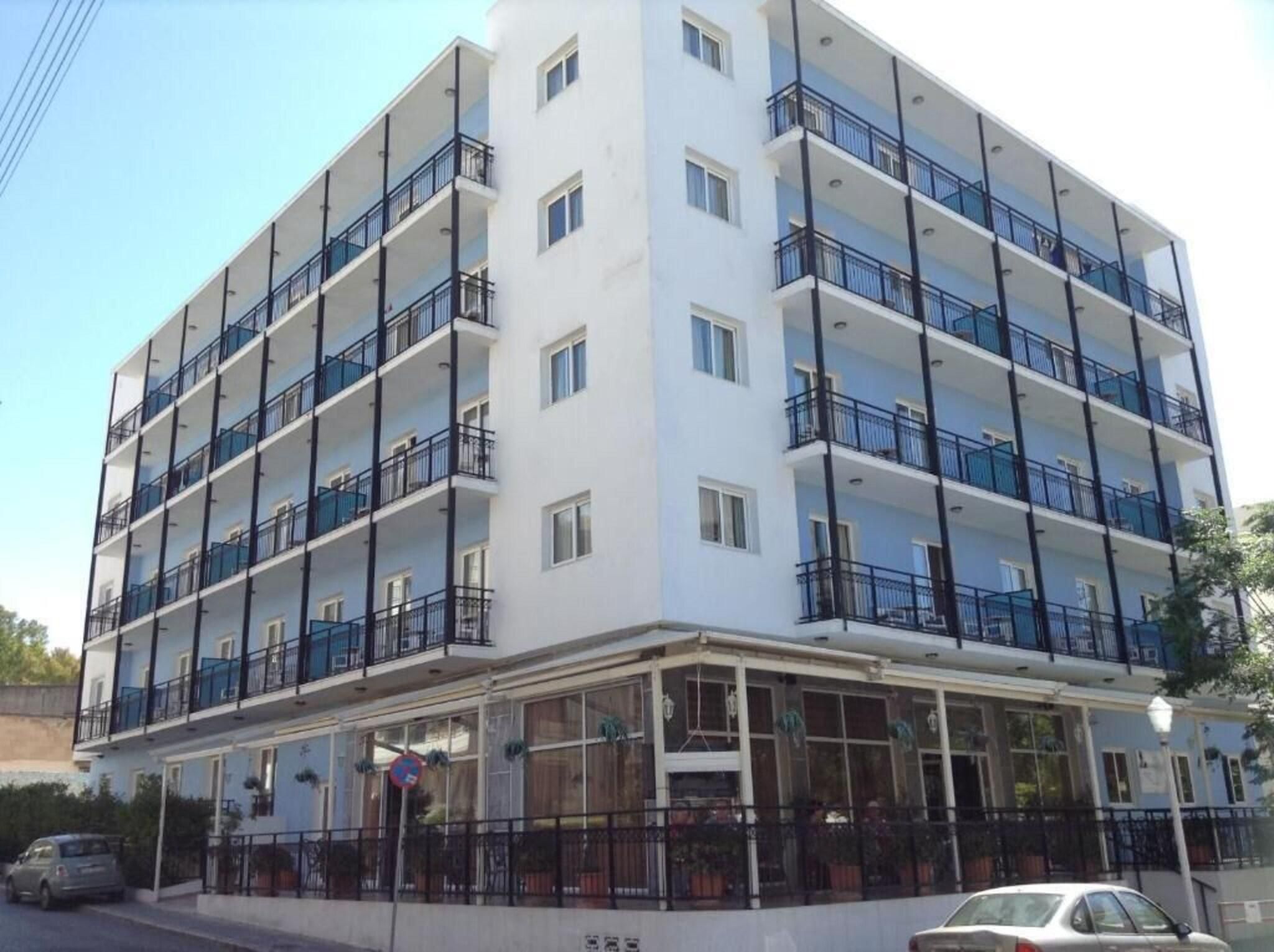 A multi-story hotel with balconies, a covered entrance, and a parking area.