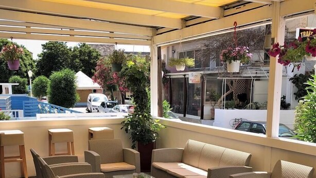 An outdoor seating area with wicker furniture, a glass table, and hanging plants. - Mimosa Suites (Rhodes)