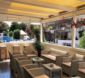 An outdoor seating area with wicker furniture, a glass table, and hanging plants. - Mimosa Suites (Rhodes)