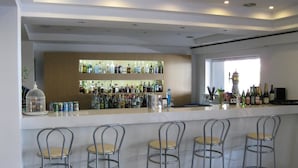 A bar area with a white countertop, metal bar stools, and a variety of bottles and cans. - Mimosa Suites (Rhodes)