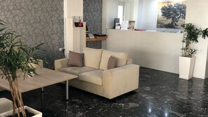 A modern living room with a beige sofa, a coffee table, and a dining table. There is a potted plant and a painting on the wall. - Mimosa Suites (Rhodes)
