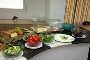 A buffet setup with various food items including bread, tomatoes, cucumbers, and cheese. - Mimosa Suites (Rhodes)