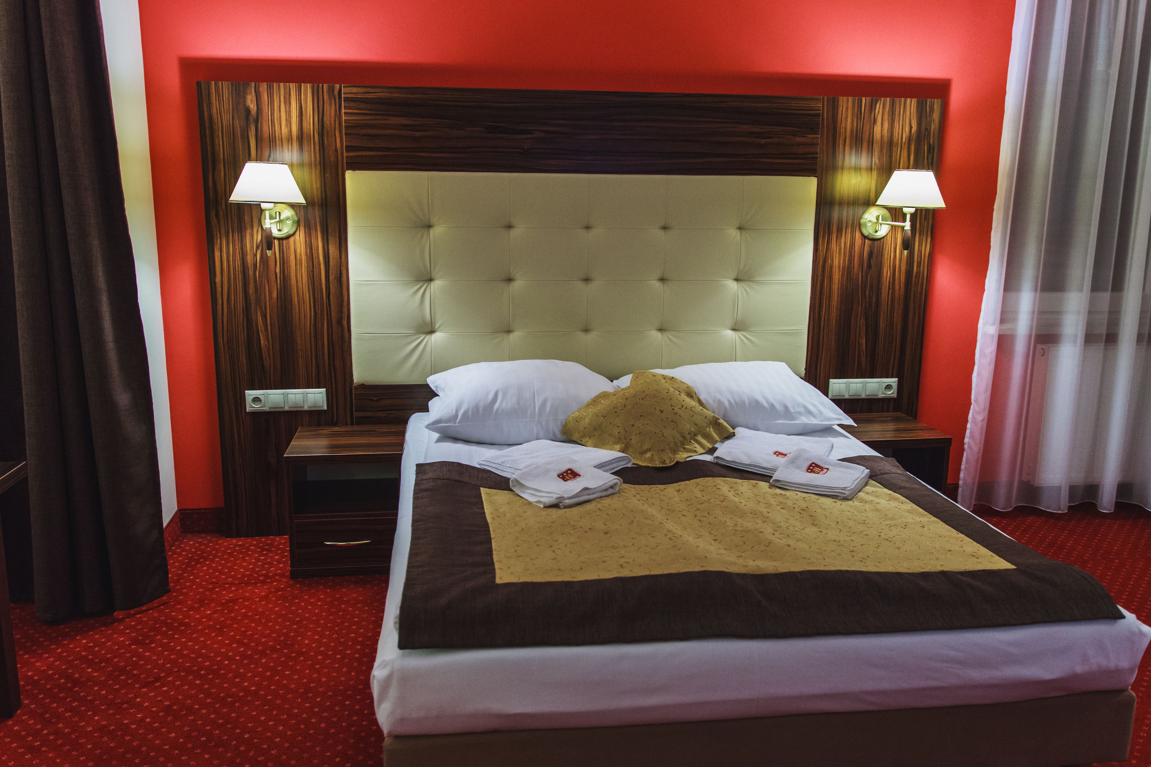 A hotel room with a large bed, two bedside tables, and a red carpet.