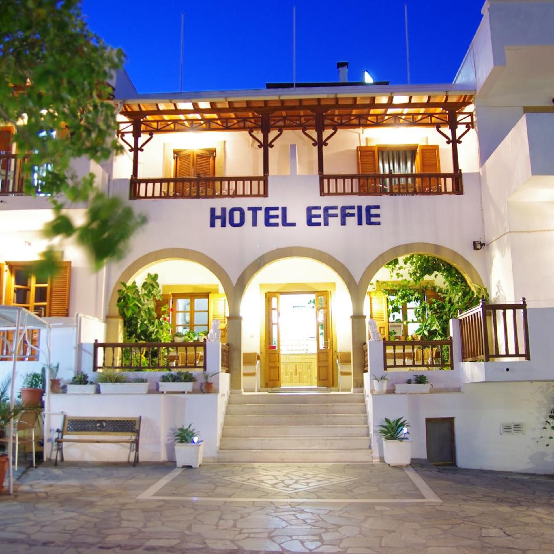 Entrada de hotel con un cartel que dice 'HOTEL EFFIE', un porche cubierto con barandas de madera y un área de acceso empedrada con piedra.