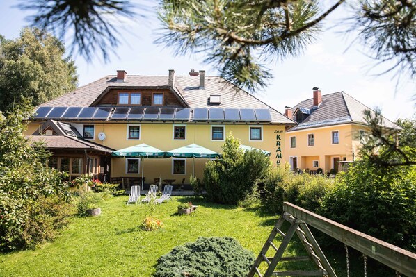Un edificio amarillo con paneles solares, mesas al aire libre y una terraza de madera.