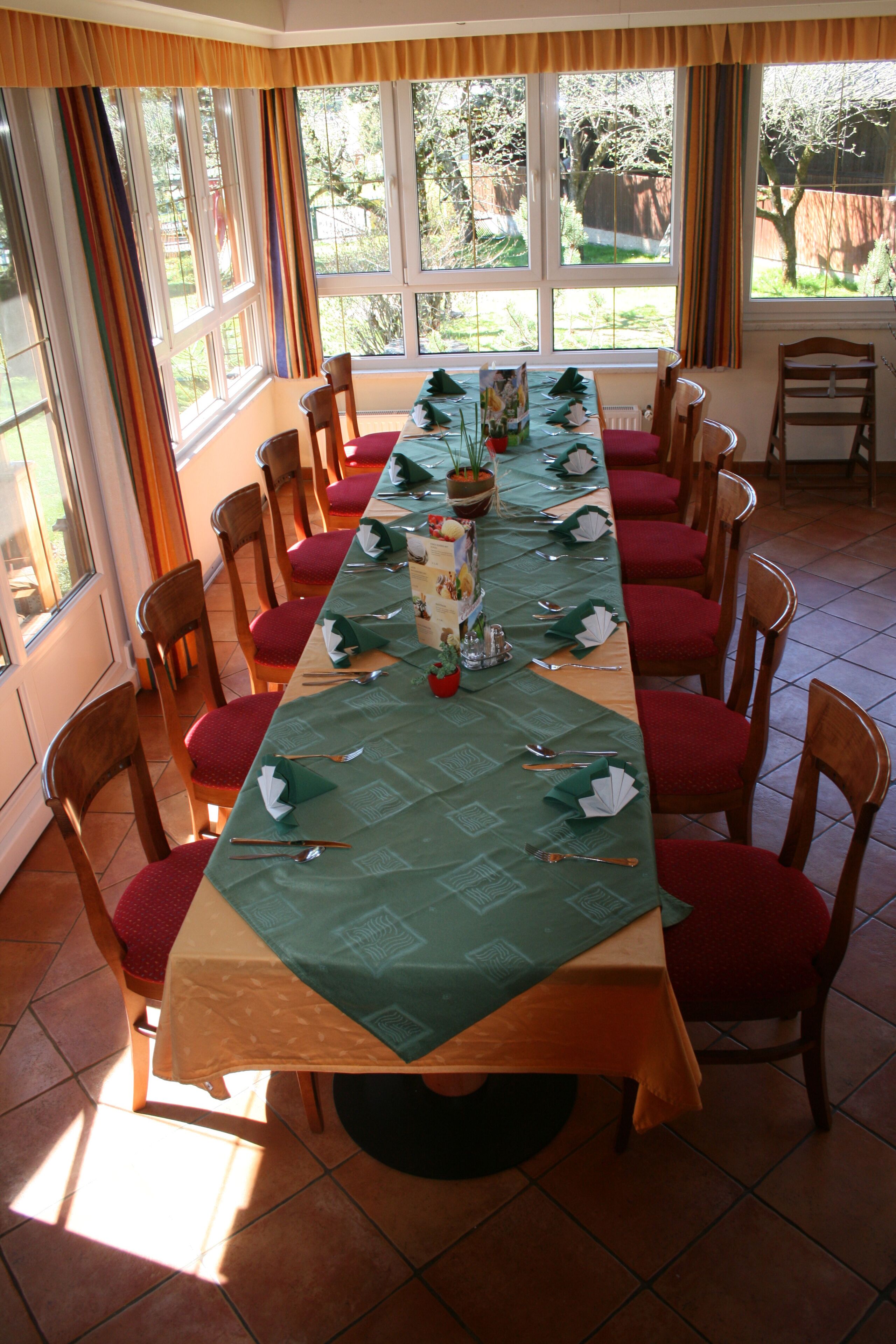 Een lange eettafel gedekt voor een maaltijd, met rode bekleden stoelen, een groene tafelkleed en een bloevas.
