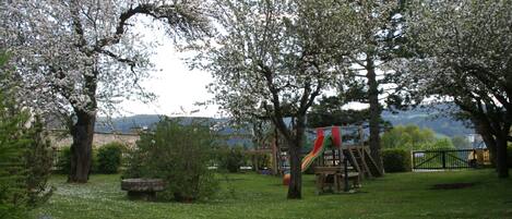 A park with a playground, trees, and a distant view of buildings.