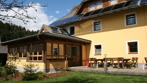 A yellow building with a sloped roof, large windows, and a wooden deck with benches. - Gasthof ZUM KRAMER (Gurk)