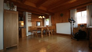 A wooden interior with a dining table and chairs, a radiator, and an exercise bike. - Gasthof ZUM KRAMER (Gurk)