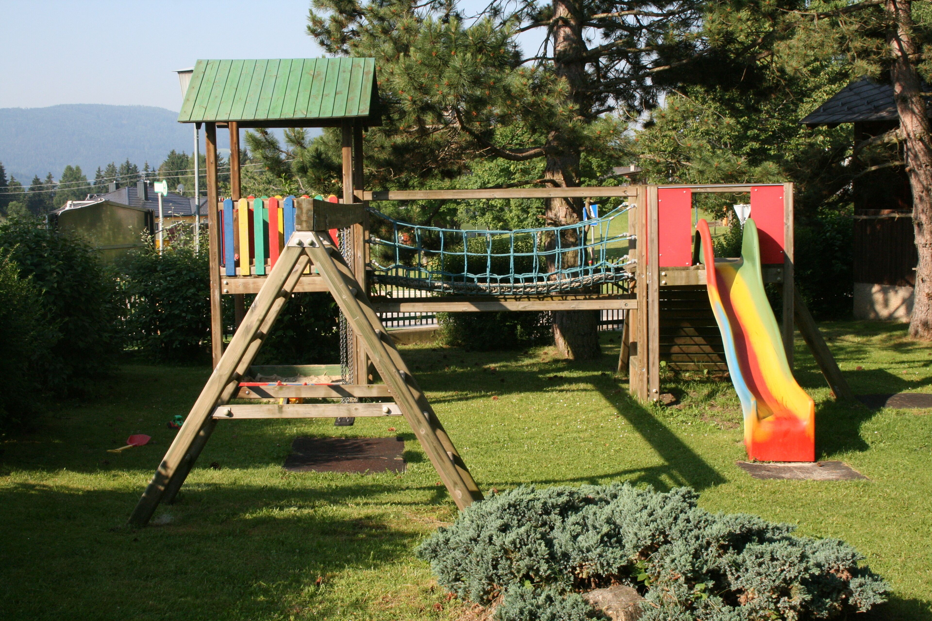 Una estructura de juego de madera con un puente de cuerda y un tobogán en un parque con césped.