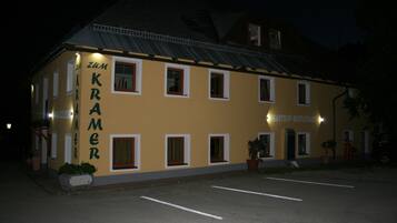 A building with the sign "Zum Kramer" and "Gasthof Restaurant" indicating it is a restaurant. There are multiple windows and a door, and the building is lit at night.