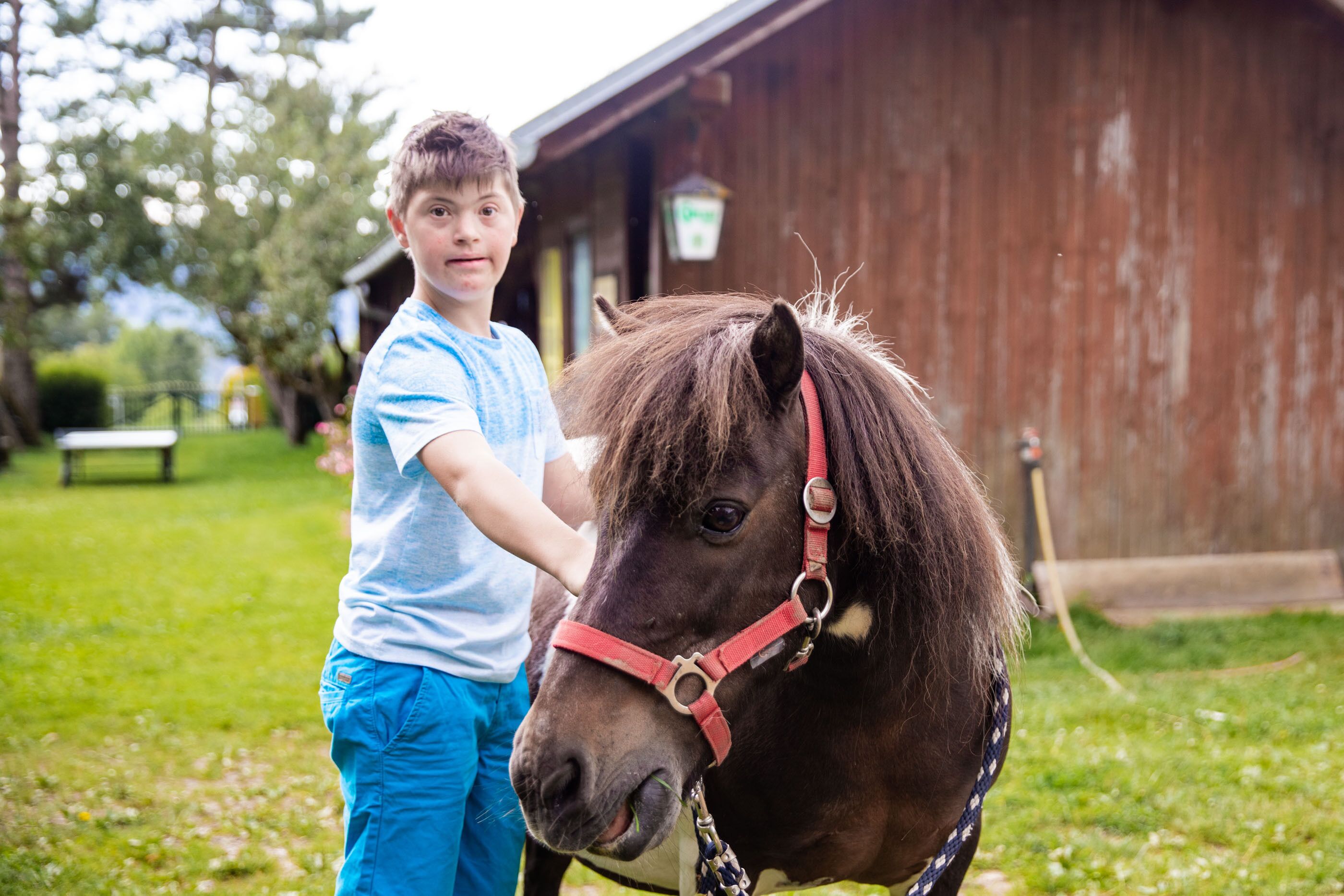 A person standing next to a horse in a grassy area with a wooden building in the background.