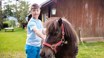 A person standing next to a horse in a grassy area with a wooden building in the background.