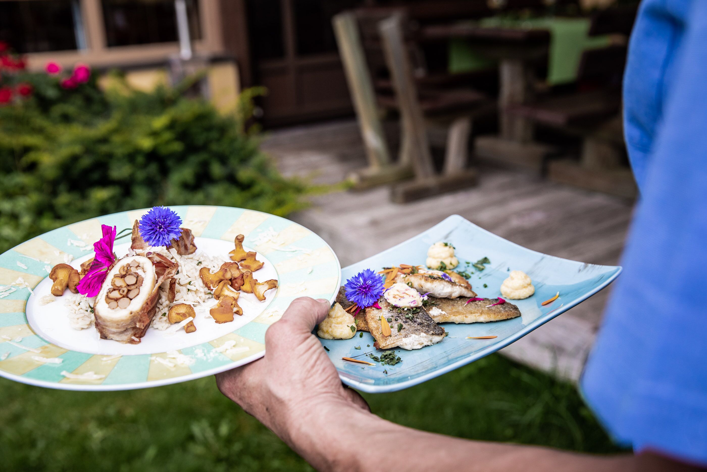 Una persona sosteniendo dos platos de comida con un jardín al fondo.