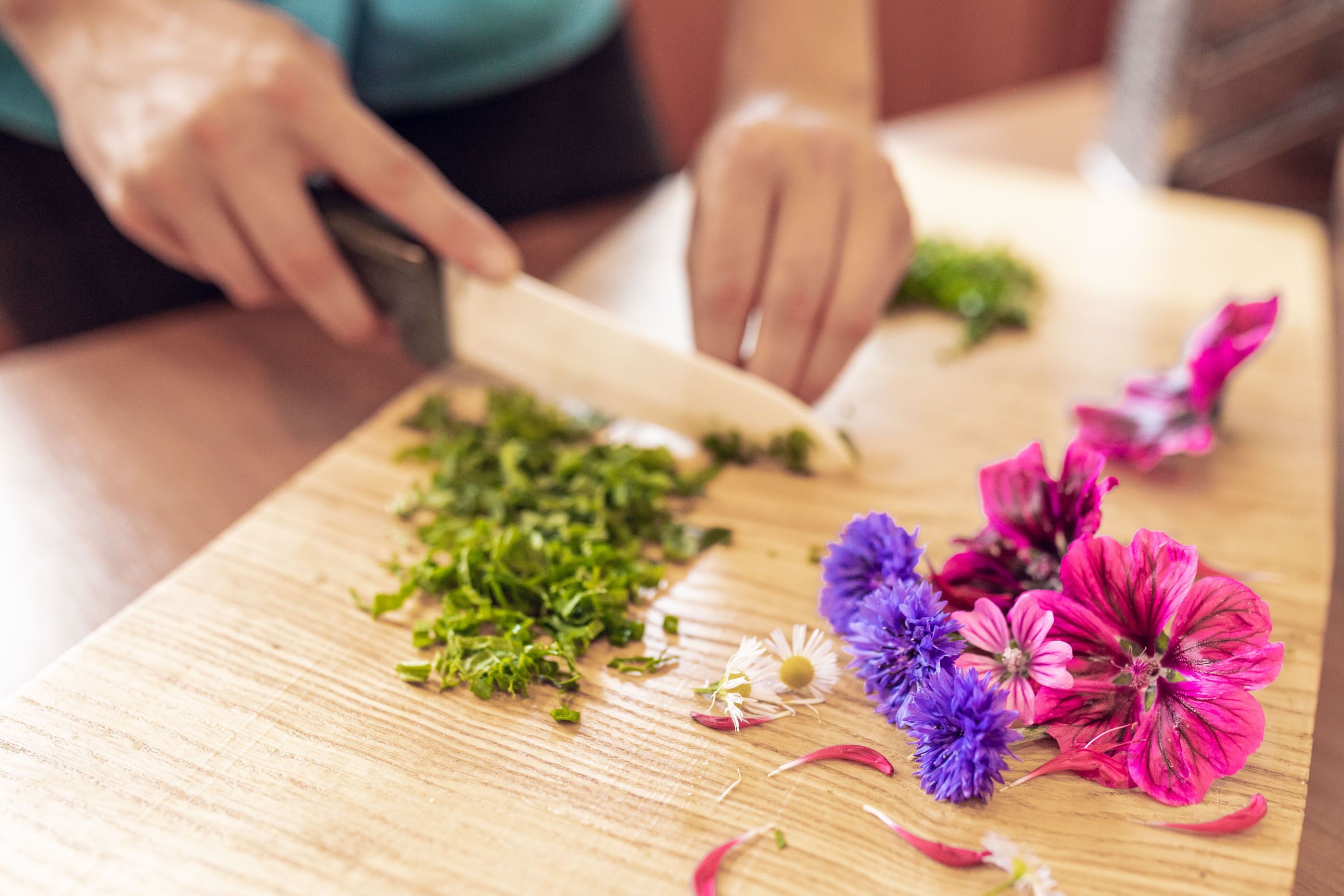 A person chopping herbs on a wooden cutting board with flowers nearby.