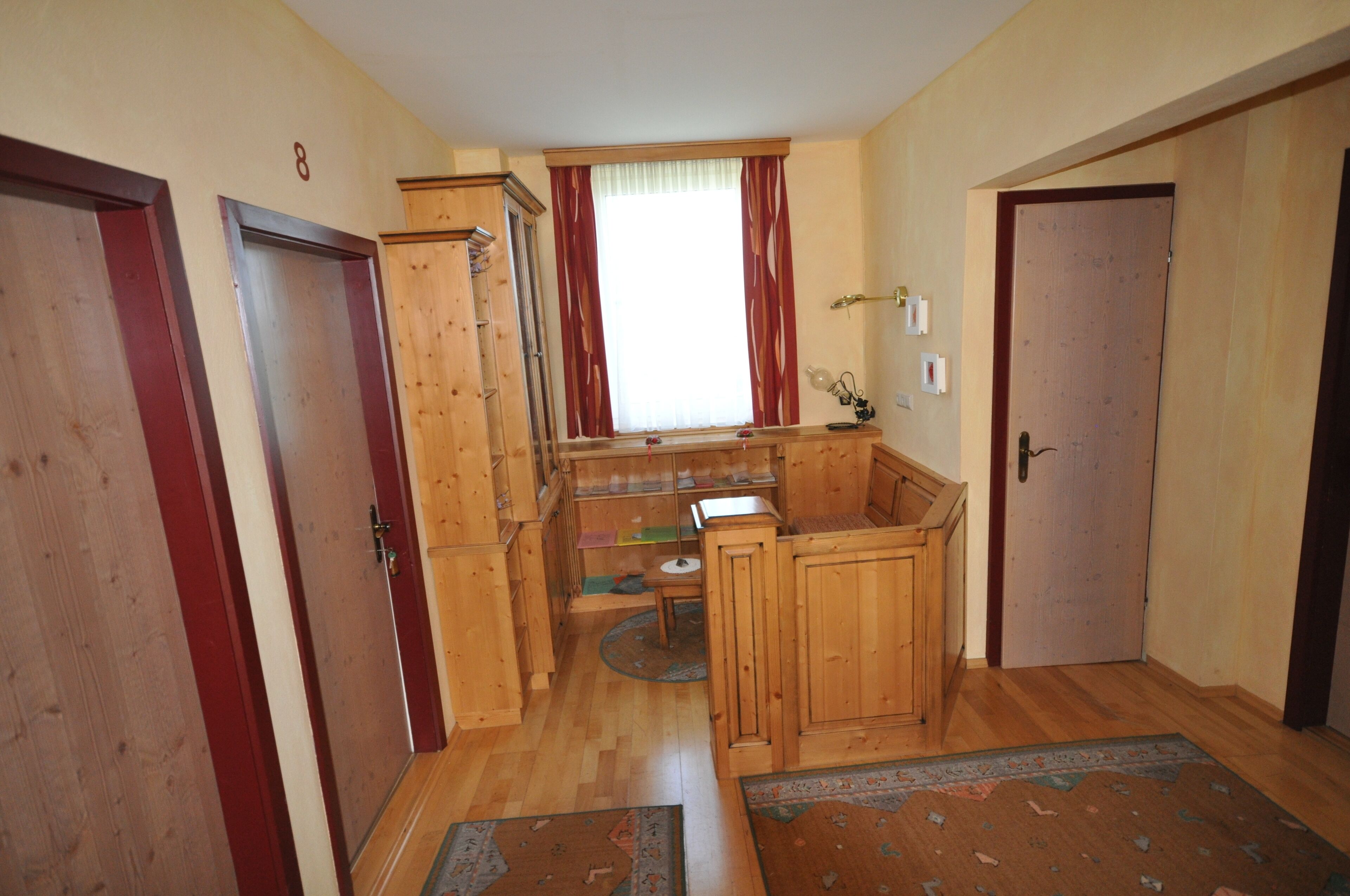 A compact kitchen with wooden cabinets, a window with red curtains, and a small dining area.