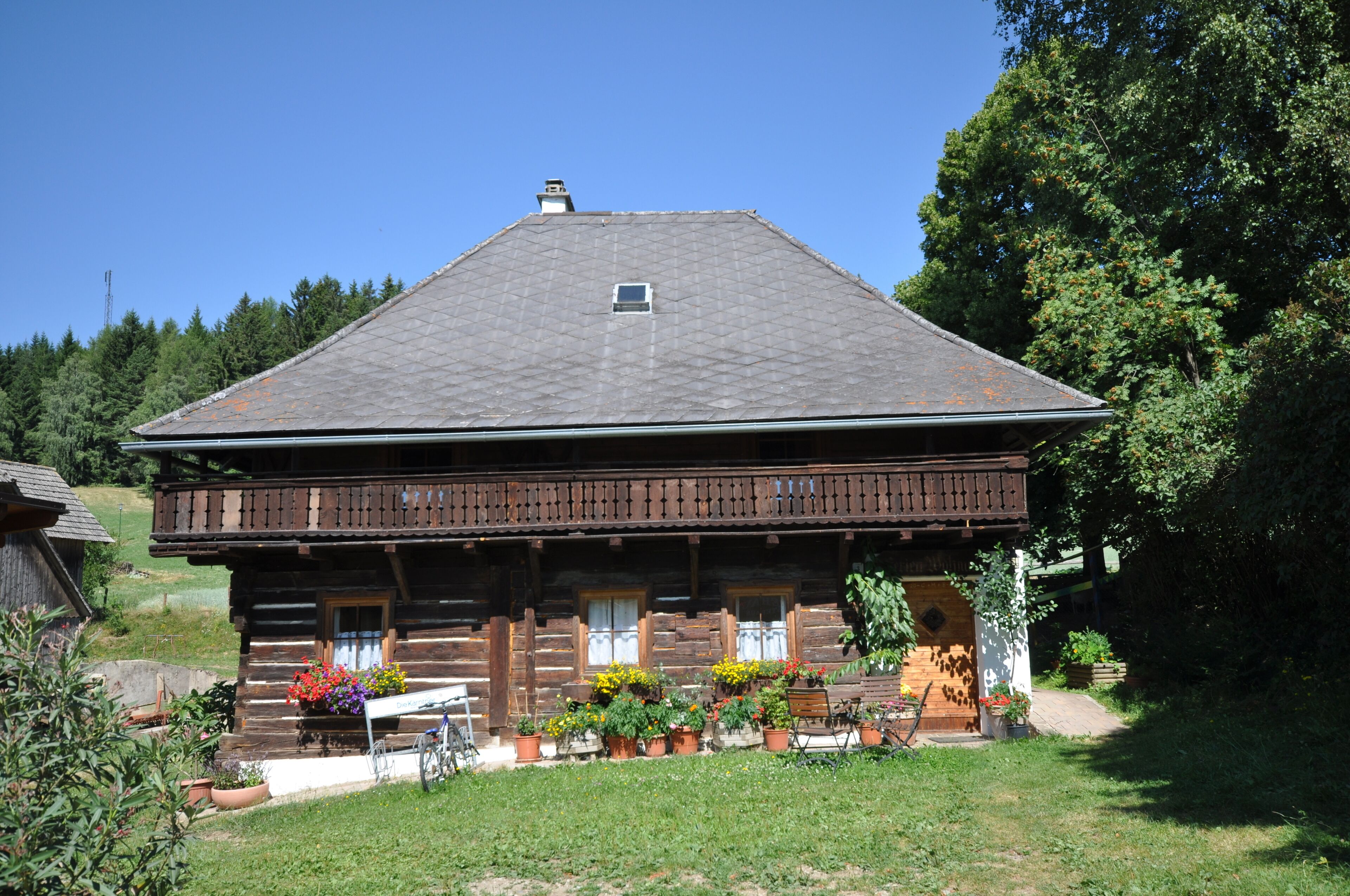 Une cabane en rondins de bois dotée d’un balcon, entourée de plantes en pot et d’un vélo.