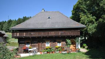 Une cabane en rondins de bois dotée d’un balcon, entourée de plantes en pot et d’un vélo.
