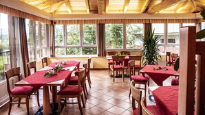 A dining area with wooden tables and chairs, large windows, and a wooden ceiling. - Gasthof ZUM KRAMER (Gurk)