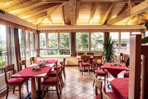 Un comedor con mesas y sillas de madera, ventanas amplias y techo de madera.
