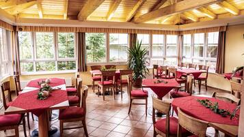 Een restaurant met houten balken, rode tafelkleden en meerdere ramen met uitzicht op het landschap.