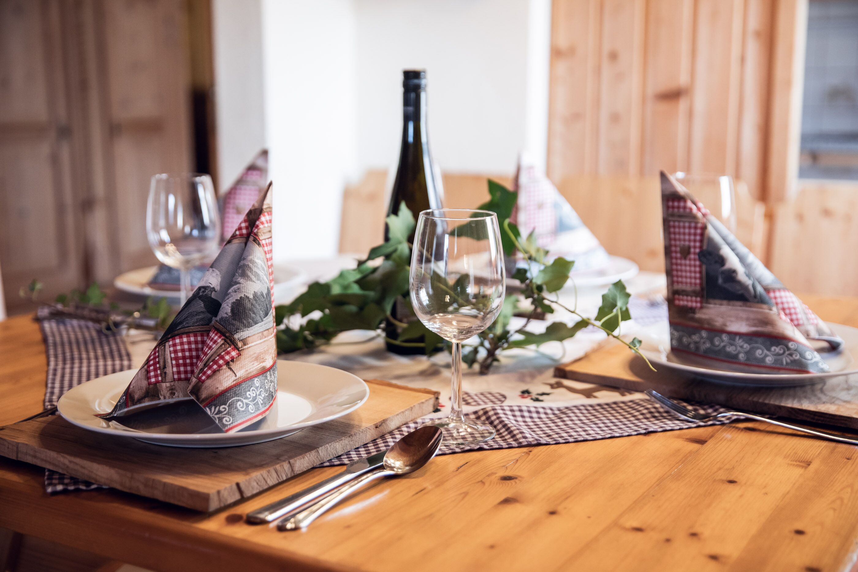 Una mesa de madera para comer con una botella de vino, copas y servilletas dobladas con forma de barcos.