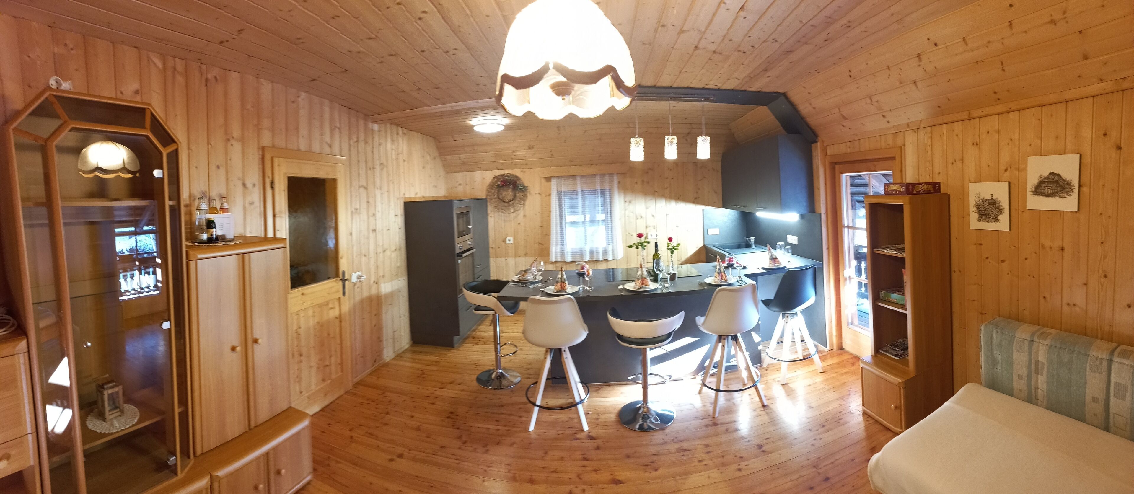 A wooden interior with a central island, bar stools, a dining table, and a sofa.