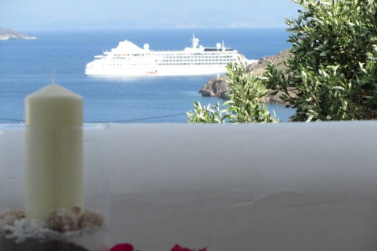 Una mesa blanca con vela y flores, con vista a un crucero en el mar.