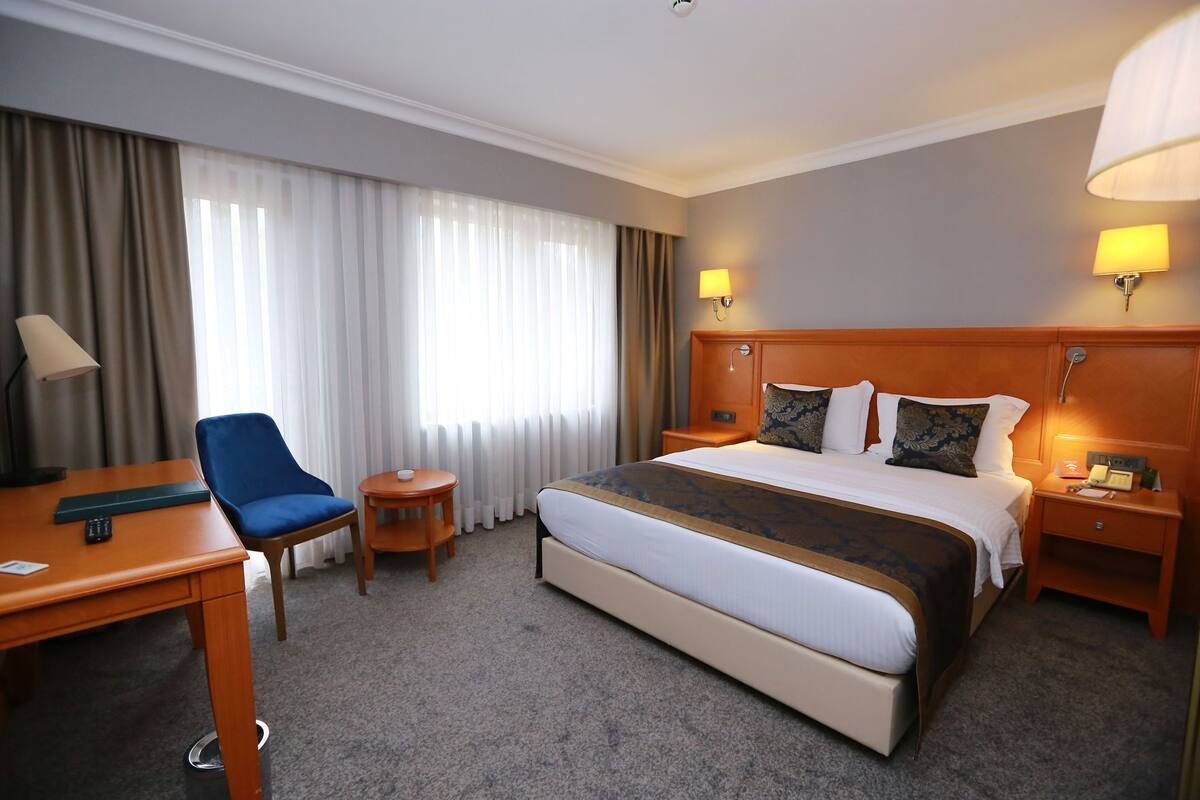 Ein Hotelzimmer mit einem großen Bett, einem Schreibtisch, einem Sessel, einem kleinen Tisch und einer Lampe.