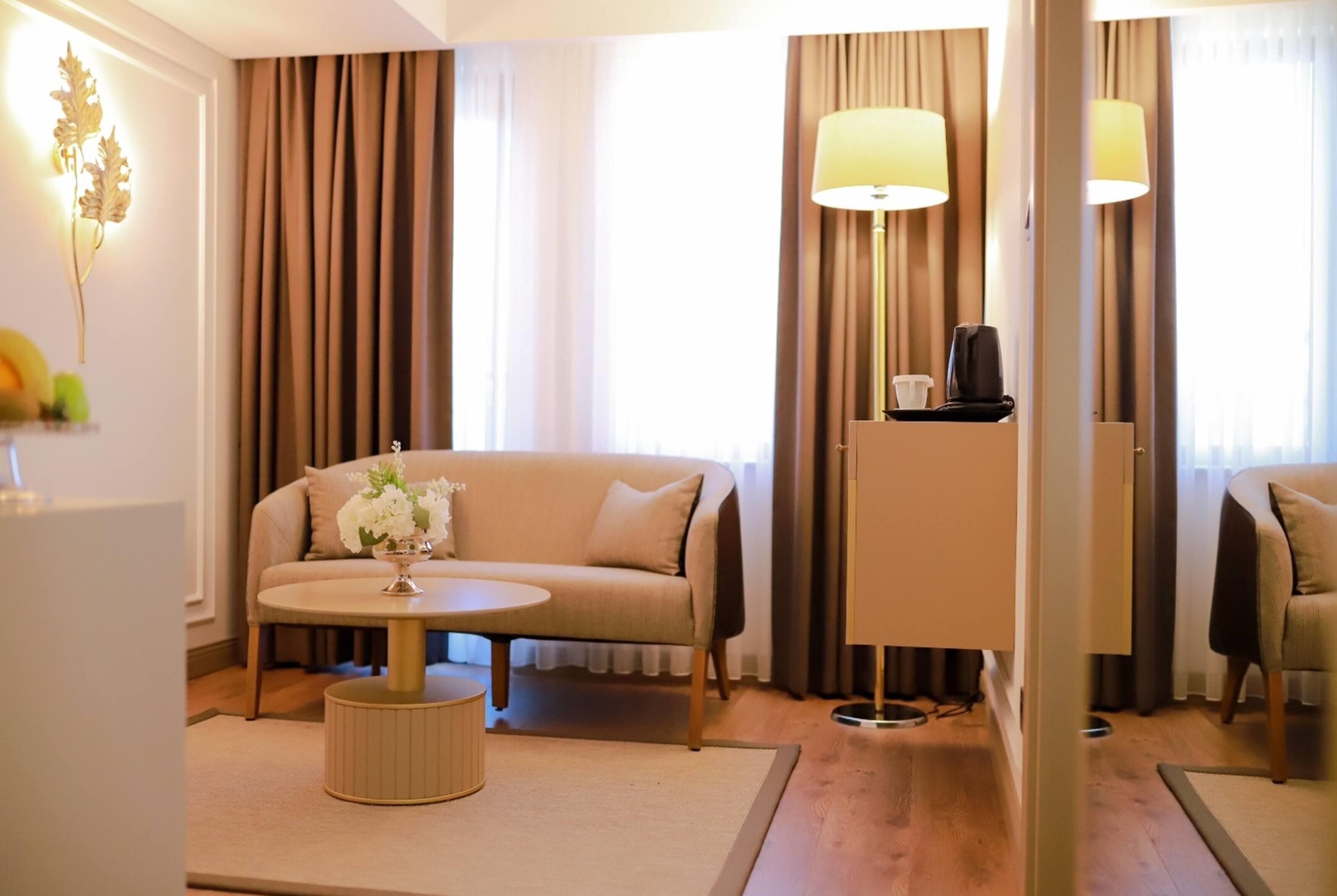 A hotel room with a sofa, a round table, a lamp, and a small cabinet.