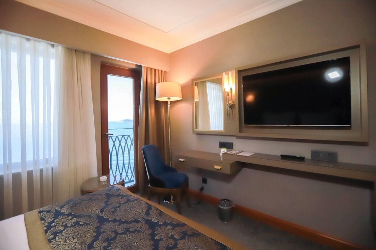 Ein Hotelzimmer mit Bett, Schreibtisch, Stuhl, Fernseher und einem fensterbepflanzten Fenster.