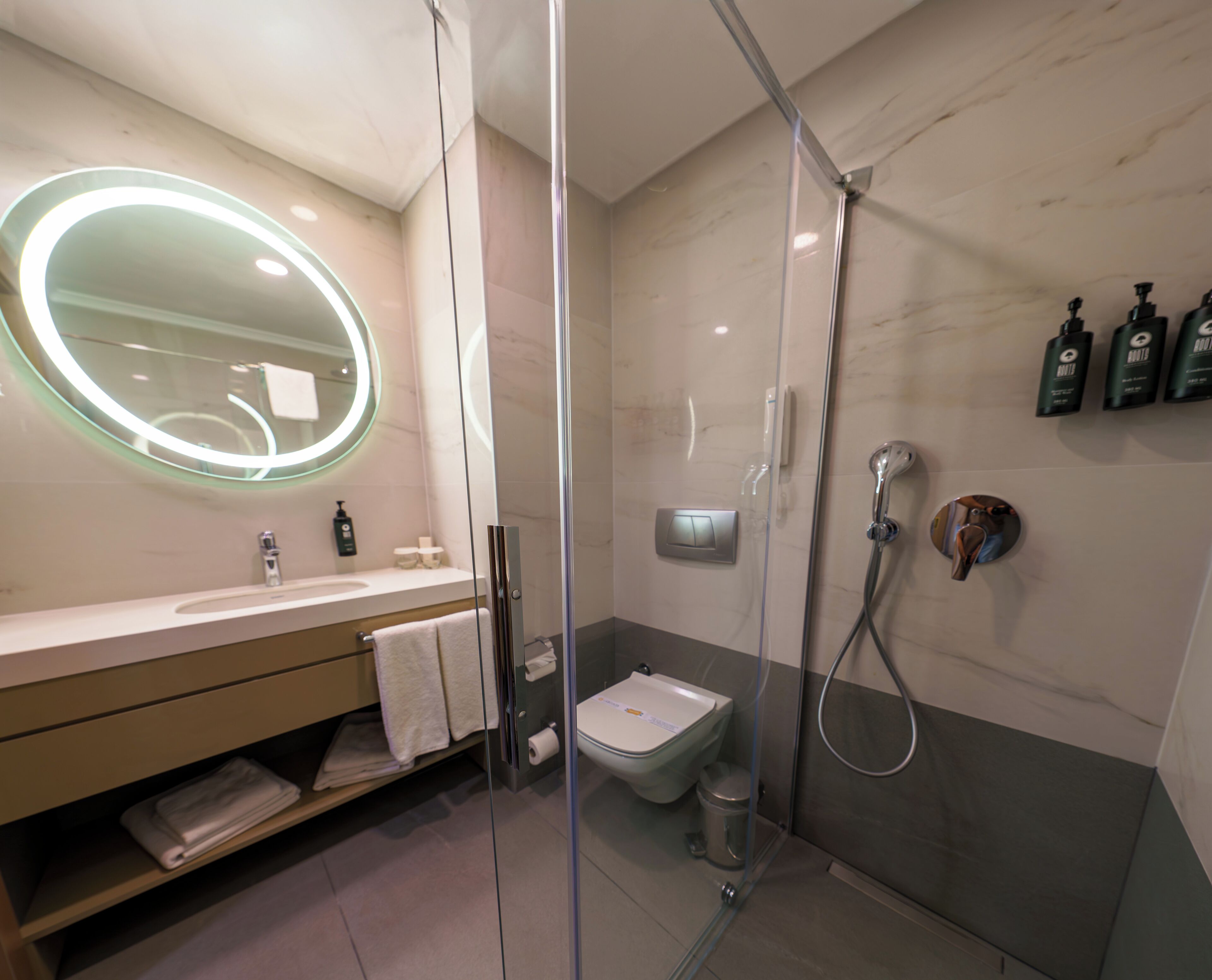 A modern bathroom with a glass-enclosed shower, a round mirror, a toilet, and a sink with a vanity.