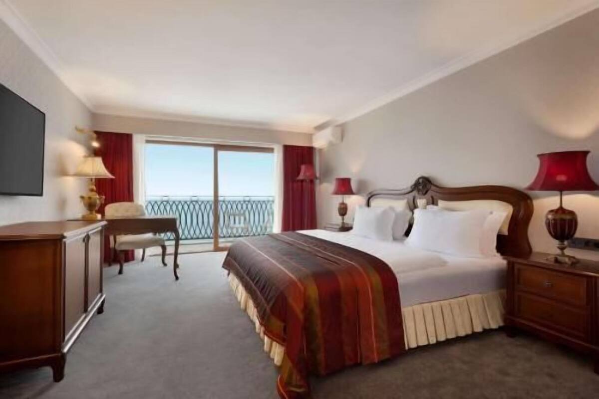 Ein Hotelzimmer mit Bett, Nachttischen, Schreibtisch und Stuhl. Ein Balkon bietet einen Ausblick.
