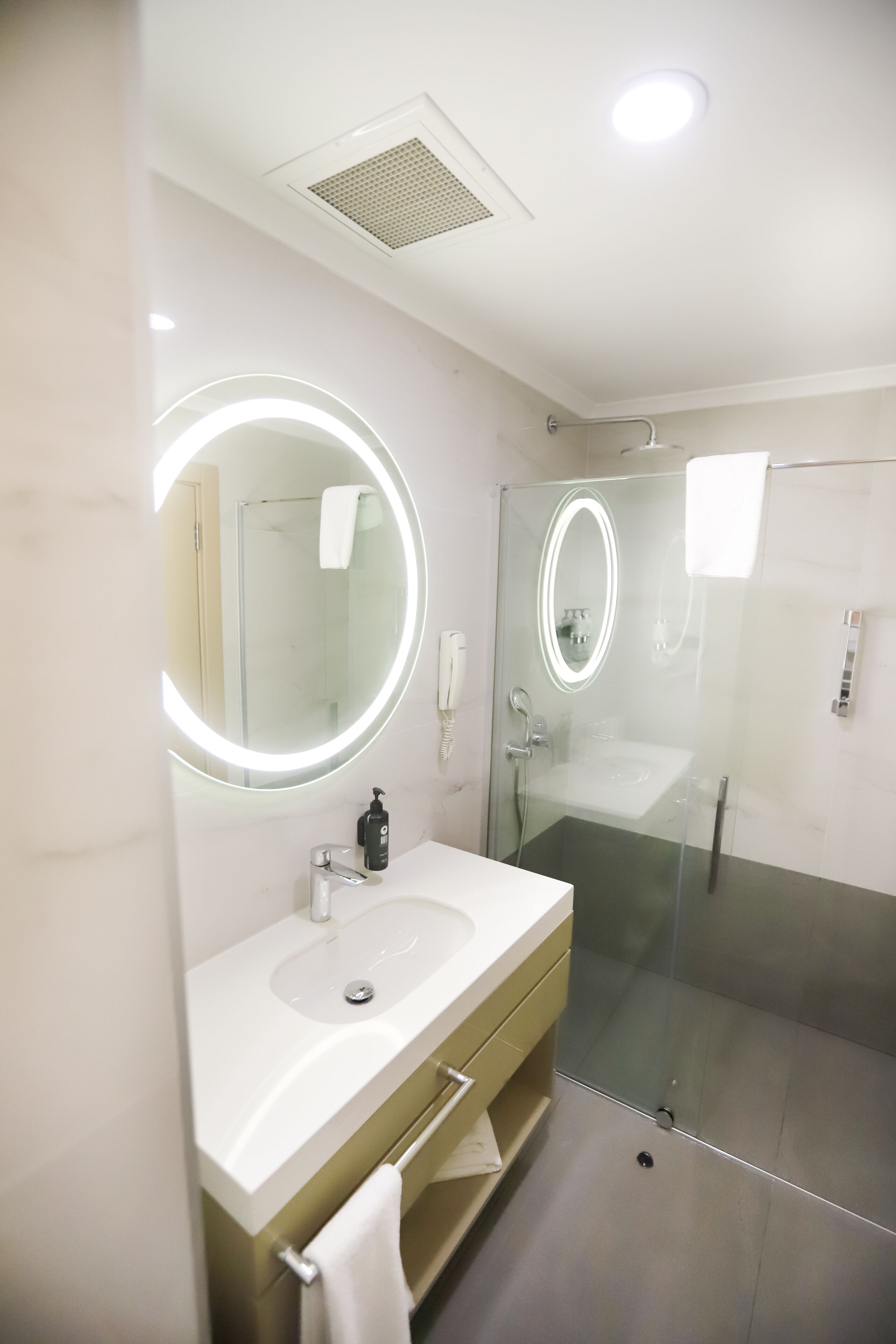 A modern bathroom with a round mirror, a sink, and a glass-enclosed shower.